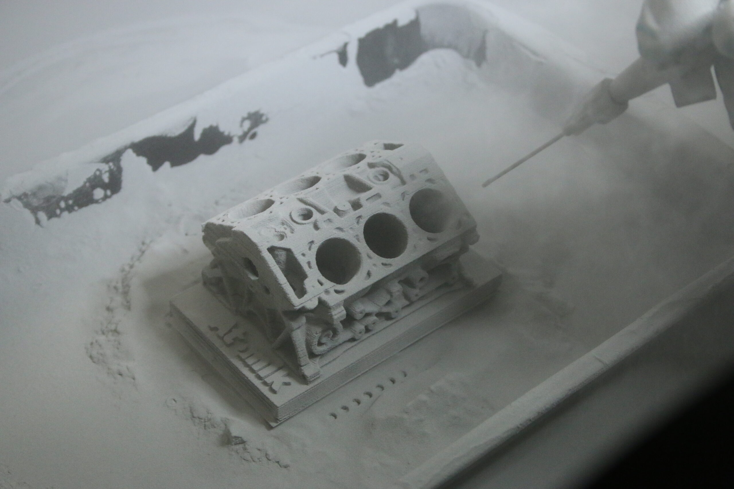 3D printed engine block being cleaned in a powder bed after binder jetting.